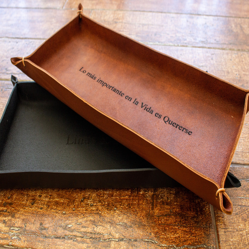 One black and one whiskey brown oblong trays, crafted by hand from Italian full-grain leather, personalized with engraved names.