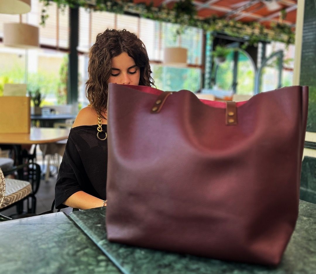 Woman sitting at a table with a large bordo tote bag in front of her.