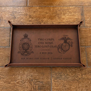 Brown leather tray with engraved text and logos on a wooden surface