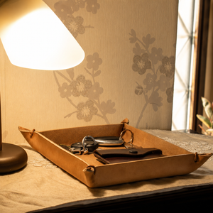 Brown leather tray with keys and wallet on a table next to a lamp.