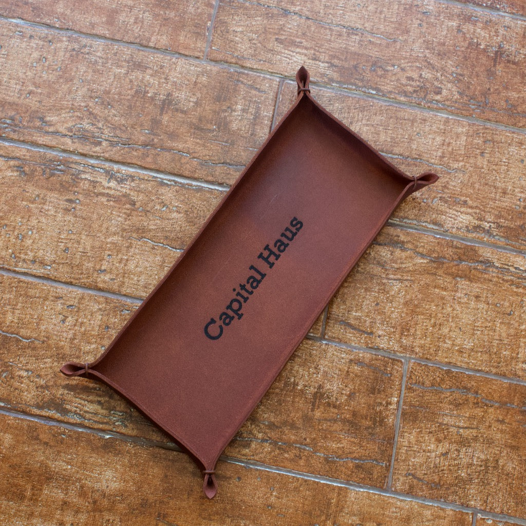 Italian full-grain leather in a brown color forms an oblong tray with leather string held corner tips and an engraved name.