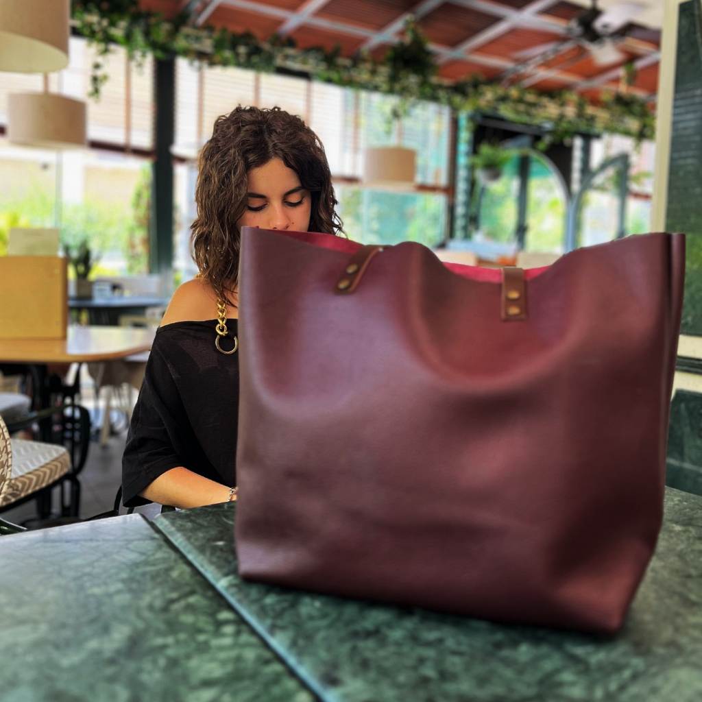 Large bordo Italian full-grain leather tote bag with dark shoulder straps and exterior pocket, designed as a stylish companion for work, errands, or relaxing moments.