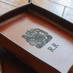 Brown leather tray with embossed crest and initials on a wooden surface.
