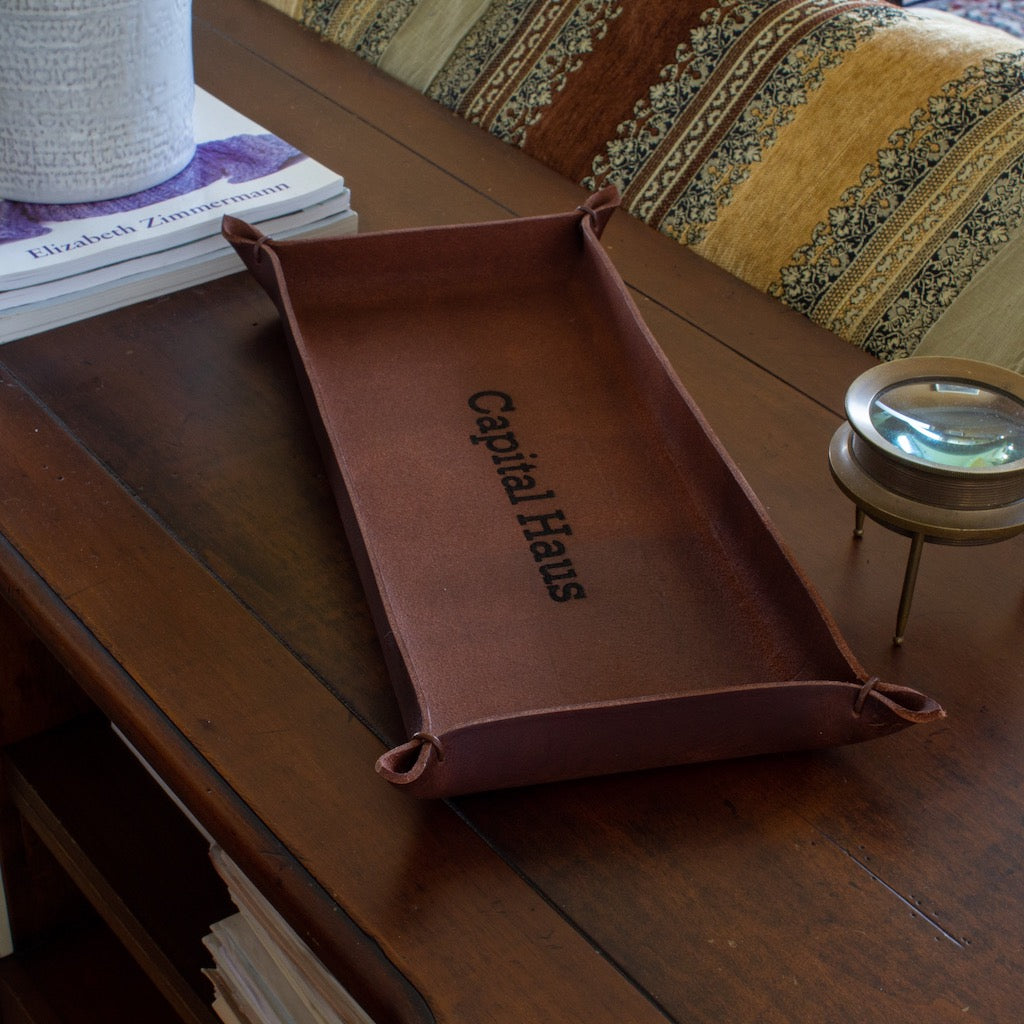 Italian full-grain leather in a brown color forms an oblong tray with leather string held corner tips and an engraved name.