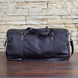 Black leather duffel bag on a wooden surface with a stone wall background