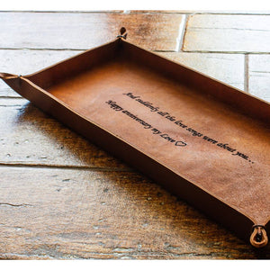 Italian full-grain leather in a whiskey brown color forms an oblong tray with leather string held corner tips and an imprinted message.